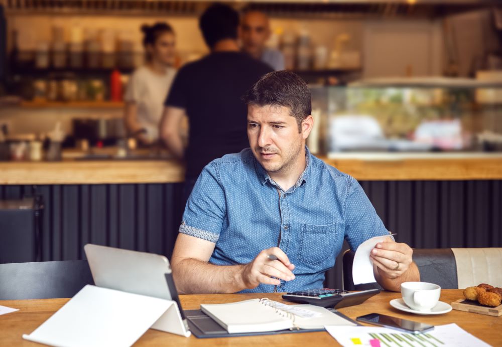 Small business owner calculating expenses sitting at a table in a restaurant 